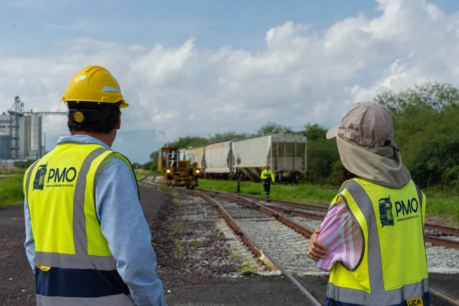 Dos integrantes del equipo de PMO observan la vía férrea de la terminal, con ferrotolvas, el remolcador ferroviario y los silos al fondo